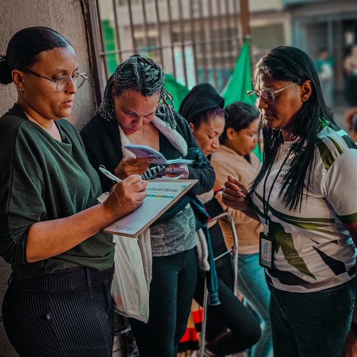 Voluntária auxilia moradoras no preenchimento de fichas de cadastro durante um atendimento.